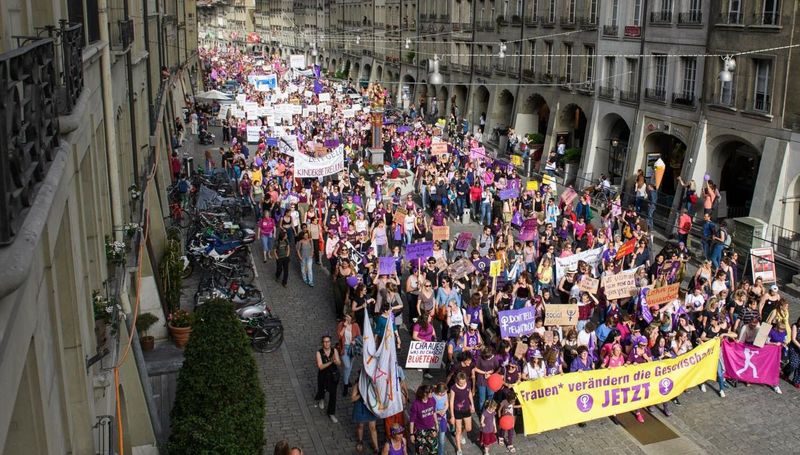 Bild der Frauensternstreikdemo in der Berner Innenstadt. Viele Teilnehmende tragen violette und Banner. Das Frontbanner trägt die Aufschrift Frauen verändern die Gesellschaft jetzt.