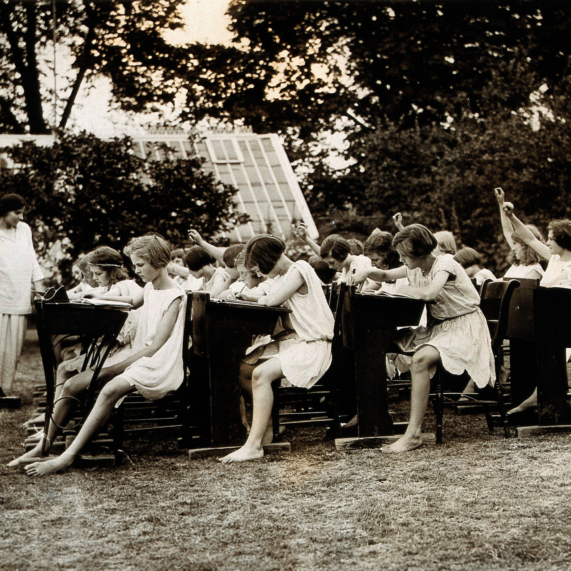 Un groupe de jeunes filles assises en plein air sur des bancs d'école suivent une leçon donnée par leur institutrice