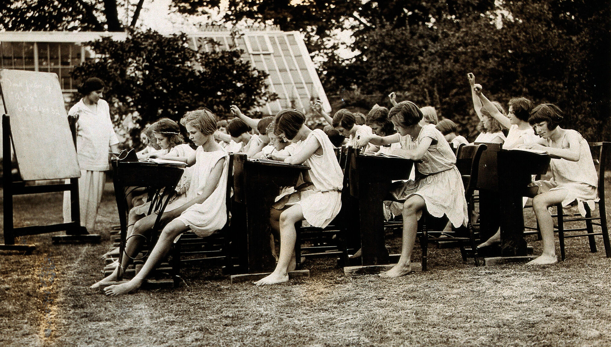Un groupe de jeunes filles assises en plein air sur des bancs d'école suivent une leçon donnée par leur institutrice