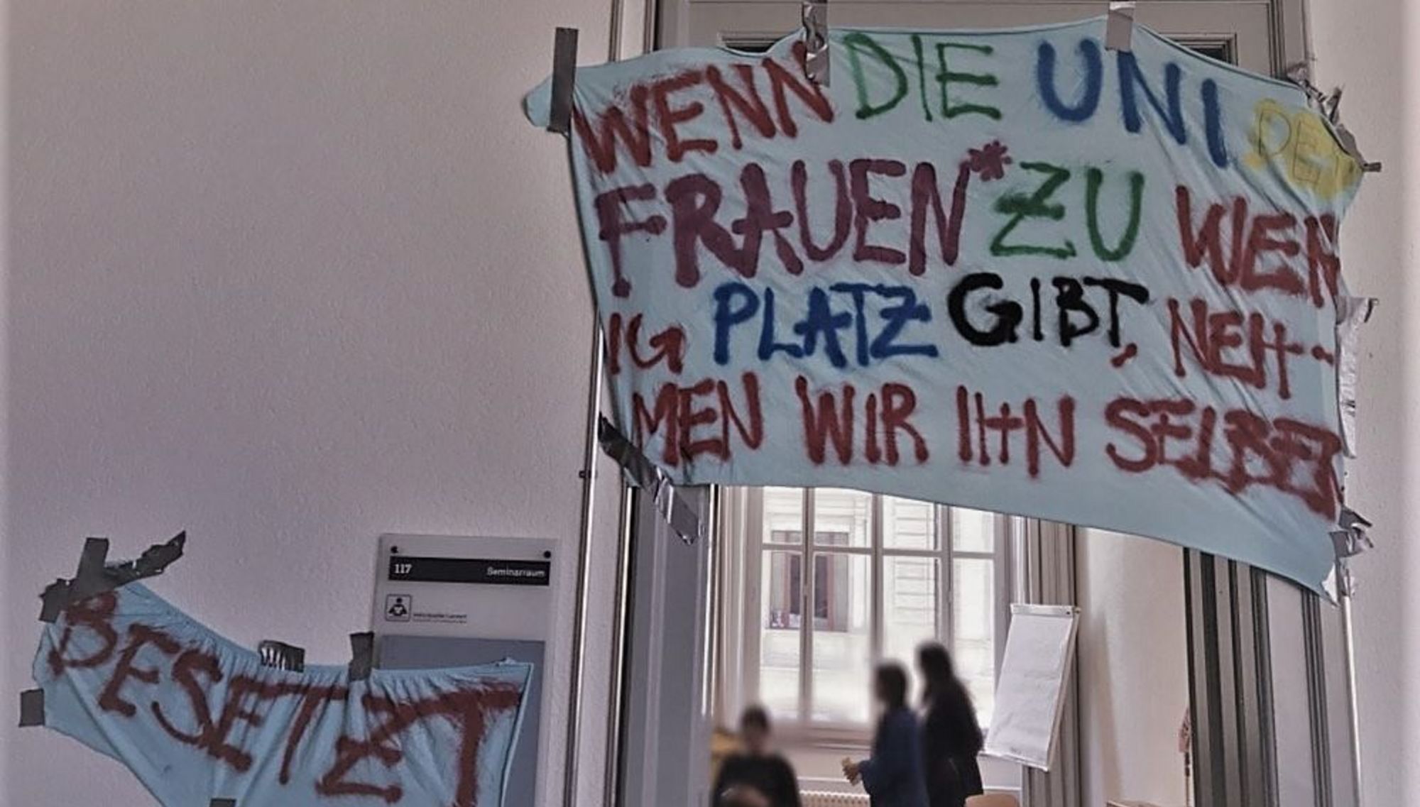 Zu sehen ist die Eingangstüre eines Raumes, der am 14. Mai an der Universität Bern besetzt wurde. Auf einem Transparent ist folgendes zu lesen: "Wenn die Uni den Frauen* zu wenig Platz gibt, nehmen wir ihn selber." 